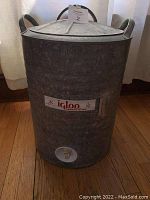 Full front view of vintage galvanized metal Igloo cooler with lid and side handles, showing spigot at bottom and Igloo branding plaque.