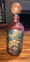 Front view of vintage bottle showing leather wrap and painted ship scene