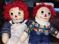 Front view of both Raggedy Ann and Andy dolls seated, showing their clothing and button eyes