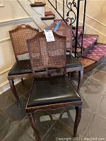 Three wooden chairs shown from a front-left angle against a stairwell, highlighting caned backs and black seats.
