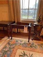View of two wooden accent tables side by side near window; one has black stone top, other has no top, with vintage samovar lamp next to it.