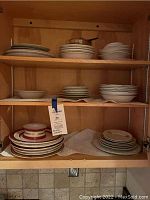 Shelf with multiple stacks of plates, bowls, and saucers in various neutral shades.