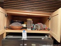Kitchen cabinet shelf with various kitchen items including blender, basket and tools inside