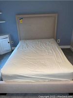 Full view of bed frame with headboard and mattress, showing beige fabric and padded construction.