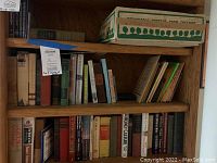 Three shelves of a wooden bookcase with multiple books of varied sizes and colors, showing spines with titles and some worn edges.