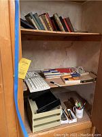 Shelf with assorted worn fiction and non-fiction books, some hardbound including The Last of the Mohicans, white computer keyboard, boxes of pencils, and small office supplies