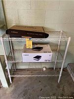 Metal shelving unit with Canon DW-100 DVD burner box and EchoGear TV wall mount box on top.