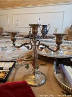 Three-arm sterling silver candelabra with ornate scrollwork arms and weighted base.