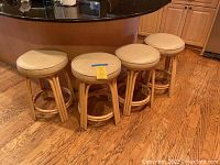 Four kitchen counter stools lined up side by side, showcasing round cream cushioned seats and rattan bases on wood floor.