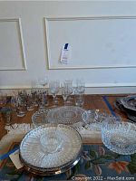 Assorted wine glasses and cut glass platters arranged on a table including a cut glass bowl and a silver-toned lazy Susan platter with cut glass inserts.