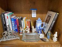Photo of a shelf showing decorative figurines including a silver-colored menorah, blue and white ceramic pitcher, and several books arranged behind them.