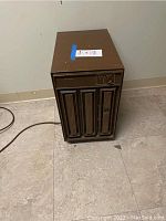 Front and side angle view of brown Kenmore dehumidifier with rectangular top and decorative front vents, power cord visible.