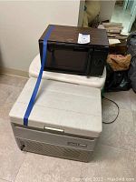 Samsung microwave on top of two coolers with blue strap securing all three items