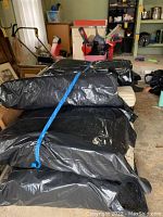 Seven patio cushions wrapped and bundled inside black plastic bags, secured with a blue strap.
