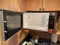 Microwave oven with the door open showing black door with mesh window and interior glass turntable.