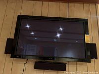 Front view of Pioneer Elite 54" TV mounted on wall with Definitive speaker system below and side speakers on either side.