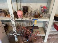 Shelf holding various vases including pink and brown ceramic, clear glass multi-necked vase, dried floral arrangement in center