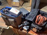 Various video and photography equipment including cameras and accessories packed in bags on a wooden bench in basement.