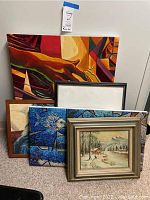 Photo showing all five paintings stacked, includes the large colorful abstract painting and various framed artworks including winter landscape and blue marine painting.