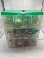Front view of three stacked plastic storage bins filled with assorted Christmas ornaments including gold wire ball ornaments and various baubles.