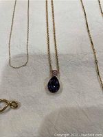 Photo showing several thin gold chains and a gold pendant with a purple tear-drop shaped gemstone.