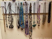Wide shot showing 18 necklaces hanging on white pegboard rack with metal hooks.