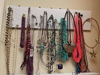Wide view of assorted necklaces hung on white pegboard rack, showing multiple colors and designs.