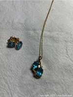 Top-down view of necklace with pendant and pair of earrings laid on white cloth.