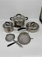 Photo showing the entire cookware set with large stockpot, wok, saucepan, mesh strainer, and steamer rack arranged on a white background.