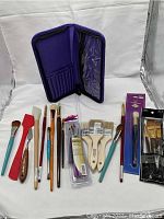 Various paintbrushes and sponges including flat, fan, and detail brushes with wooden and plastic handles in a purple case