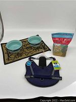 Photo of two ceramic dog bowls on decorative mat, harness, and bag of treats