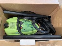 Green EuroSteam Pro Steamer with attached hose, power cord, and multiple black nozzle attachments inside cardboard box.