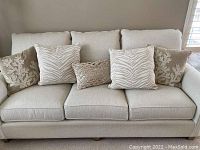 Five off white throw pillows arranged on a light beige sofa, showing two coral pattern pillows, two zebra pattern pillows, and one central textured pillow.