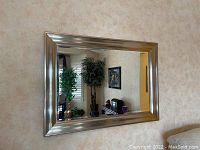 Frontal view of the full rectangular mirror with silver frame mounted on a wall, showing reflection of room.