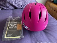 Pink Giro bike helmet with owner's manual in plastic packaging, displayed on purple fabric