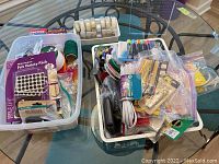 Overview of two white plastic bins filled with assorted household and office supplies including rolls of tape, felt pads, markers, and small tools.