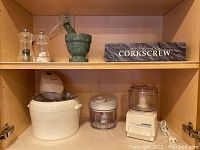 Top cabinet shelf showing green marble mortar and pestle, salt and pepper shakers, boxed professional wine bottler opener set.