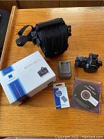 All items displayed on wood table: camera, original box, case, charger, battery, memory card, software CD