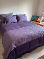 Full view of queen bed with purple sheets, pillows, bed skirt and quilted coverlet with floral patterns showing overall bedding set appearance.