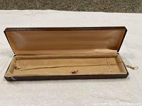 Full view of the 14k gold chain with ruby and diamond pendant and the matching ruby earrings in a beige jewelry box.