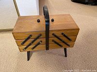 Closed wood accordion-style sewing box with black handle and legs