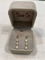 Pair of Shane Co fresh water pearl dangling earrings inside a gray velvet jewelry box with Shane Co logo on lid.