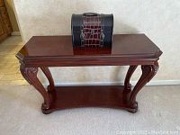 Front view of wooden sofa table with lower shelf and small chest on top.
