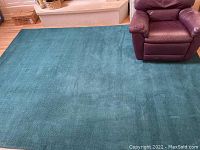 Full view of the teal blue area rug placed in a living room setting, showing size relative to nearby furniture.