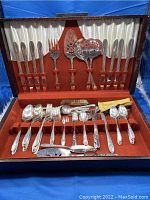 Full view of open wooden case holding Oneida Tudor Plate flatware set, showing knives, forks, spoons, and serving pieces arranged inside red velvet and white satin lining.