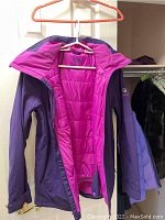 Purple outer shell jacket with bright pink insulated quilted lining and hood on hanger