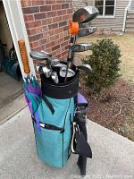 Full view of aqua golf bag with clubs, ball retriever and umbrellas