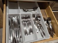 Drawer organized with knives, forks, teaspoons, tablespoons, and serving spoons separated in compartments.