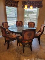 Full view of round glass-top table and six upholstered chairs in dining room