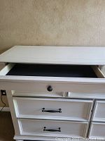 Close-up view of one open smaller top drawer showing black interior and round dark knob.